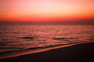 The sea after sunset has an orange glow and an orange sky with no clouds. photo