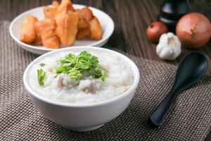 Cerdo gachas de avena con cilantro y jengibre o gachas de avena es similar a arroz gachas de avena pero mas suave en textura. servido en un de madera mesa con patongko. para desayuno en el Mañana o noche foto