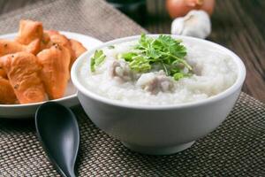 Pork porridge with coriander and ginger or porridge is similar to rice porridge but softer in texture. Served on a wooden table with patongko. For breakfast in the morning or evening photo