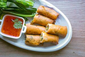 Freshly fried golden yellow spring rolls on a white plate with various vegetables and a delicious dipping sauce, top view. photo