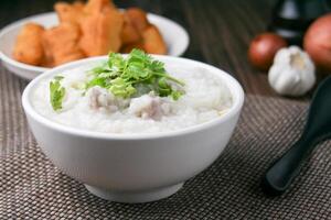 Pork porridge with coriander and ginger or porridge is similar to rice porridge but softer in texture. Served on a wooden table with patongko. For breakfast in the morning or evening photo