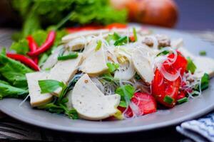 picante vaso fideos ensalada con vietnamita salchicha servido en un gris plato poner en un de madera mesa y varios vegetales. foto