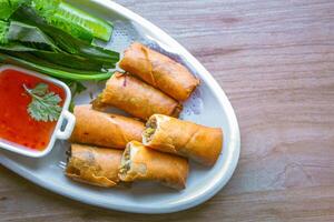 Freshly fried golden yellow spring rolls on a white plate with various vegetables and a delicious dipping sauce, top view. photo