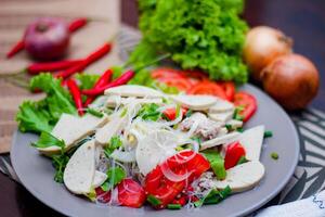 Spicy Glass Noodle Salad with Vietnamese Sausage  served in a gray plate Put on a wooden table and various vegetables. photo