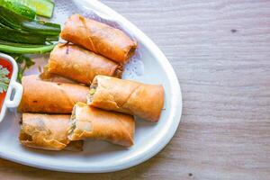 Freshly fried golden yellow spring rolls on a white plate with various vegetables and a delicious dipping sauce, top view. photo