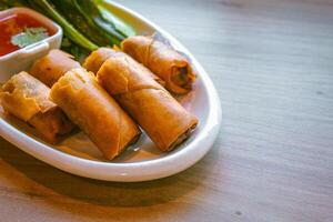 Freshly fried golden-yellow spring rolls are placed on a white plate with various vegetables and a delicious dipping sauce. photo