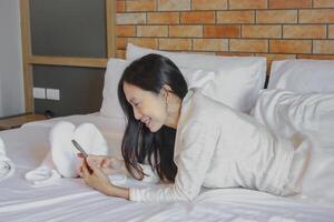 asiático mujer utilizando móvil teléfono en cama en el mañana, estilo de vida concepto. foto