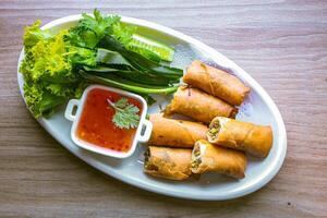 Freshly fried golden yellow spring rolls on a white plate with various vegetables and a delicious dipping sauce, top view. photo