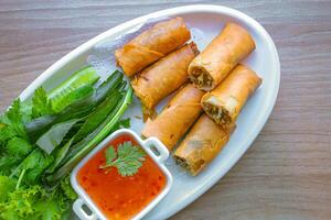 Freshly fried golden yellow spring rolls on a white plate with various vegetables and a delicious dipping sauce, top view. photo