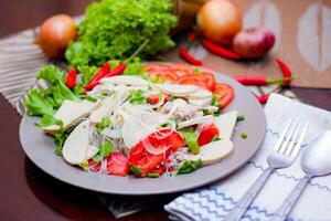 picante vaso fideos ensalada con vietnamita salchicha servido en un gris plato poner en un de madera mesa y varios vegetales. foto