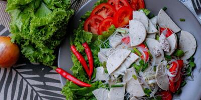 picante vaso fideos ensalada con vietnamita salchicha servido en un gris plato poner en un de madera mesa y varios vegetales. foto