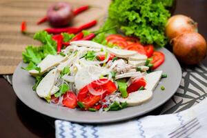 Spicy Glass Noodle Salad with Vietnamese Sausage  served in a gray plate Put on a wooden table and various vegetables. photo