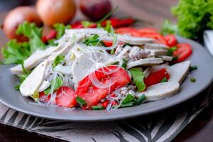 Spicy Glass Noodle Salad with Vietnamese Sausage  served in a gray plate Put on a wooden table and various vegetables. photo