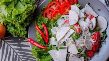 picante vaso fideos ensalada con vietnamita salchicha servido en un gris plato poner en un de madera mesa y varios vegetales. foto