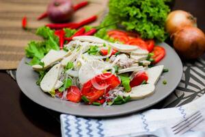 Spicy Glass Noodle Salad with Vietnamese Sausage  served in a gray plate Put on a wooden table and various vegetables. photo