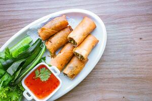 Freshly fried golden yellow spring rolls on a white plate with various vegetables and a delicious dipping sauce, top view. photo