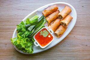 Freshly fried golden yellow spring rolls on a white plate with various vegetables and a delicious dipping sauce, top view. photo