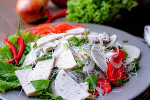 Spicy Glass Noodle Salad with Vietnamese Sausage  served in a gray plate Put on a wooden table and various vegetables. photo