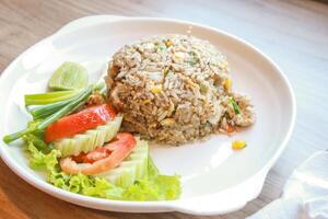 Pork fried rice served in a restaurant with wooden floor tables with tomatoes, cucumbers, scallions, fried rice, delicious food made from steamed rice. photo