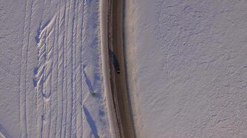 Suv rides on road through the snowy field. Aerial view on a snowy field and road from quadrocopter. Aerial view of snowy fields and road video