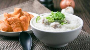 Cerdo gachas de avena con cilantro y jengibre o gachas de avena es similar a arroz gachas de avena pero mas suave en textura. servido en un de madera mesa con patongko. para desayuno en el Mañana o noche foto