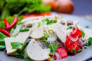 Spicy Glass Noodle Salad with Vietnamese Sausage  served in a gray plate Put on a wooden table and various vegetables. photo