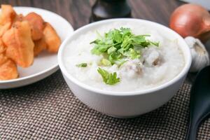 caliente chino gachas de avena arroz gachas de avena con picado Cerdo albóndigas para desayuno en un de madera mesa. foto