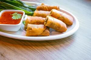 Freshly fried golden-yellow spring rolls are placed on a white plate with various vegetables and a delicious dipping sauce. photo