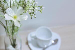 blanco flores en un florero en el mesa con un taza de café foto