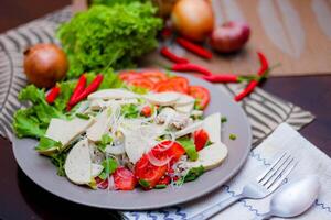 picante vaso fideos ensalada con vietnamita salchicha servido en un gris plato poner en un de madera mesa y varios vegetales. foto