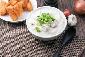 Hot Chinese porridge rice porridge with minced pork meatballs for breakfast on a wooden table. photo