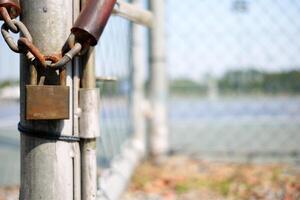 Old Rusty Padlock Hanging on Chain with Blurred Metal Fence Background. photo