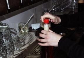 detrás el encimera. De las mujeres manos hermosamente y fácilmente verter cerveza dentro un botella. foto