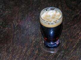 A mug of dark beer foaming on a wooden table. photo