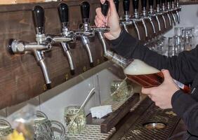 detrás el encimera. De las mujeres manos hermosamente y fácilmente verter cerveza dentro un botella. foto