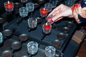 Prayer candles inside a Catholic church. A woman's hand holds a candle. photo