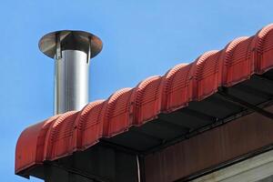 Stainless Chimney on Red Roof with Blue Sky Background. photo