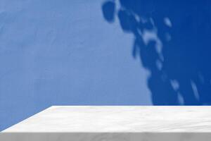 White Marble Table Corner with Light Beam, Shadow, and Spotlight on the Blue Concrete Wall Background, Suitable for Product Presentation Backdrop, Display, and Mock up. photo