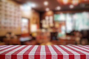 vacío mesa cubierto con rojo a cuadros Manteles y borroso restaurante antecedentes. foto