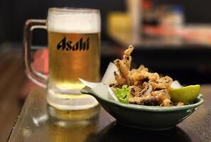 bangkok, Tailandia septiembre 28, 2023 ika gesso karaage o profundo frito calamar tentáculos con asahi cerveza antecedentes en madera mesa en japonés restaurante. eso es repartido por asahi cervecerías, limitado. foto