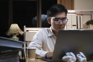 joven empresario trabajando tiempo extraordinario en un escritorio a noche. foto