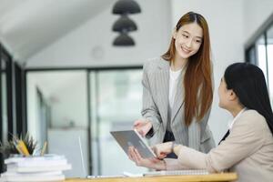 Office woman is standing and teaching a new employee. It describes the work format displayed on the tablet screen. photo