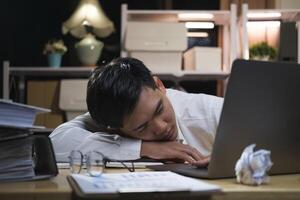 joven cansado empresario acostado en mesa a noche oficina. foto