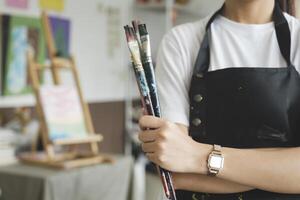 A close-up of the artist hands wearing an apron smeared with paint. Clutching many brushes and paintbrushes. photo