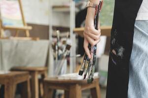 A close-up of the artist hands wearing an apron smeared with paint. Clutching many brushes and paintbrushes. photo