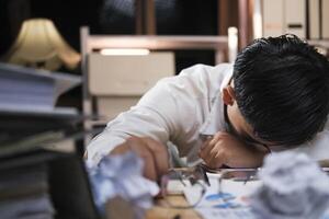 Young tired businessman lying on table at night office. photo