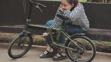 Chilling and relaxed young Asian woman in casual comfy clothes riding a bicycle on the bike lane in the park. hobby and exercise concept video