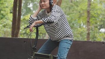 chillen en ontspannen jong Aziatisch vrouw in gewoontjes comfortabel kleren rijden een fiets Aan de fiets rijbaan in de park. hobby en oefening concept video