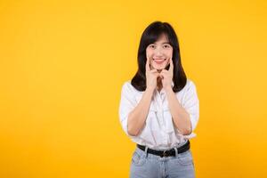 Young beautiful asian woman happy smile wearing white shirt and denim jean plants over yellow isolated background smiling confident showing and pointing with fingers teeth and mouth. Dental concept. photo