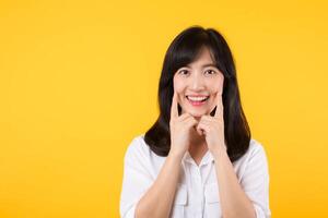 Young beautiful asian woman happy smile wearing white shirt and denim jean plants over yellow isolated background smiling confident showing and pointing with fingers teeth and mouth. Dental concept. photo